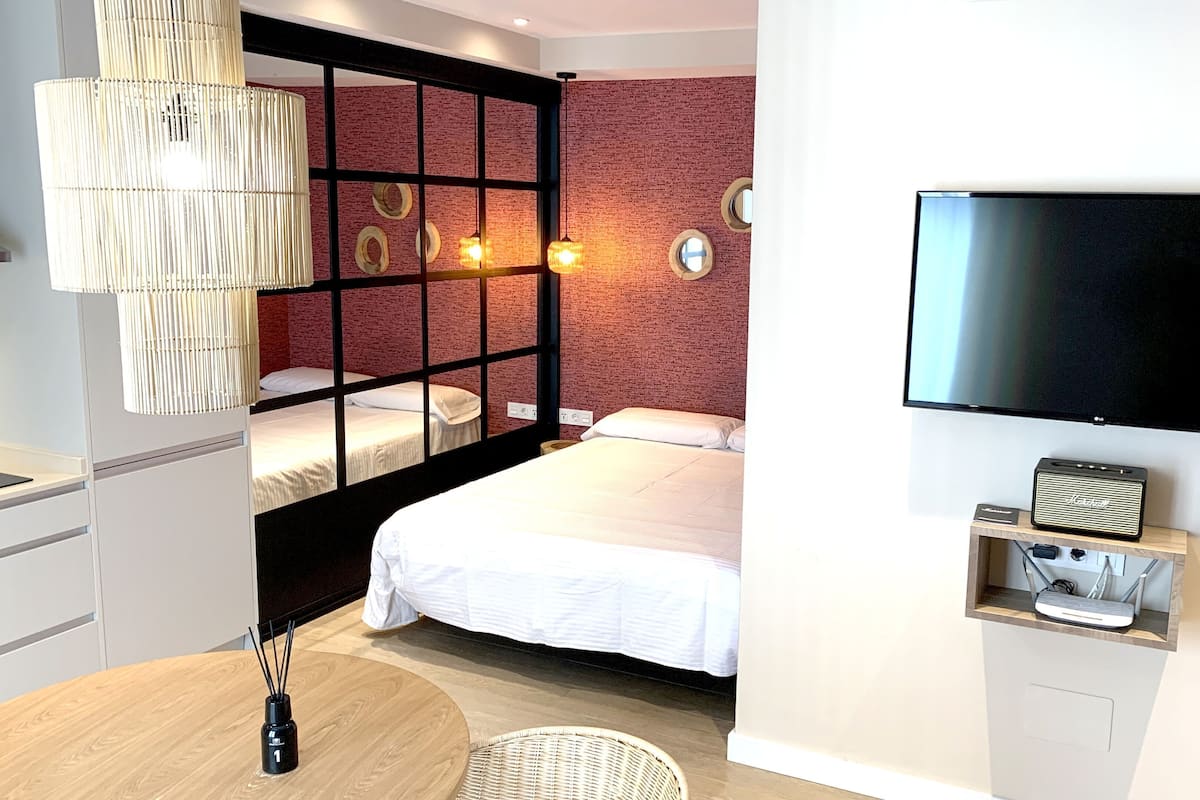 Una habitació d'hotel moderna amb un llit, una televisió, una taula petita i una cadira de vimet.