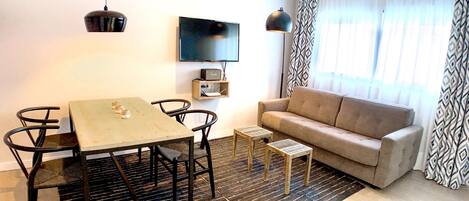 Una sala de estar con un sofá, un televisor, una mesa y dos mesitas auxiliares.