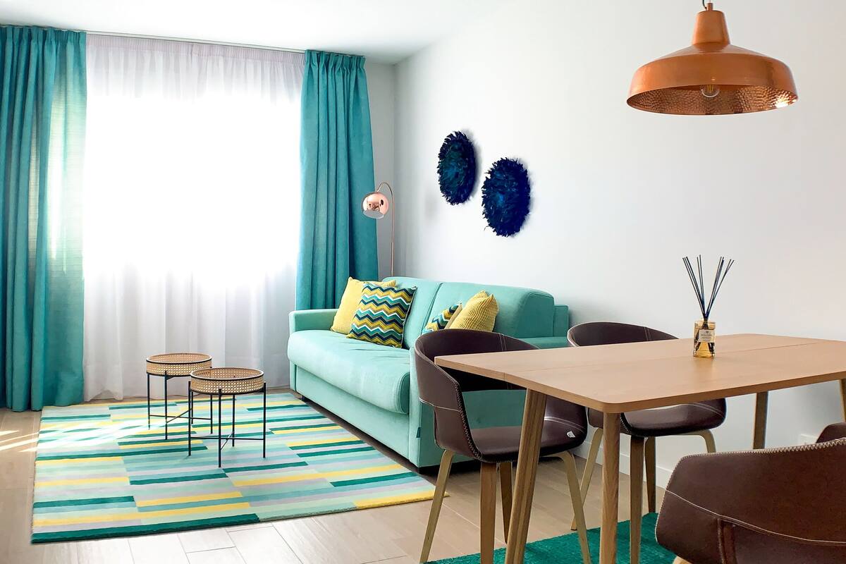 Un saló modern amb un sofà color turquesa, una taula de menjador de fusta i un televisor fixat a la paret.