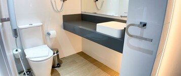 A modern bathroom with a toilet, a trash bin, a sink, and a mirror.