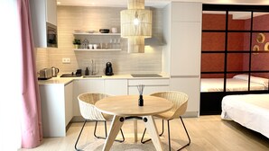 Een moderne hotelkamer met een keukenhoek, een eettafel met stoelen, een bed en een groot raam met gordijnen.