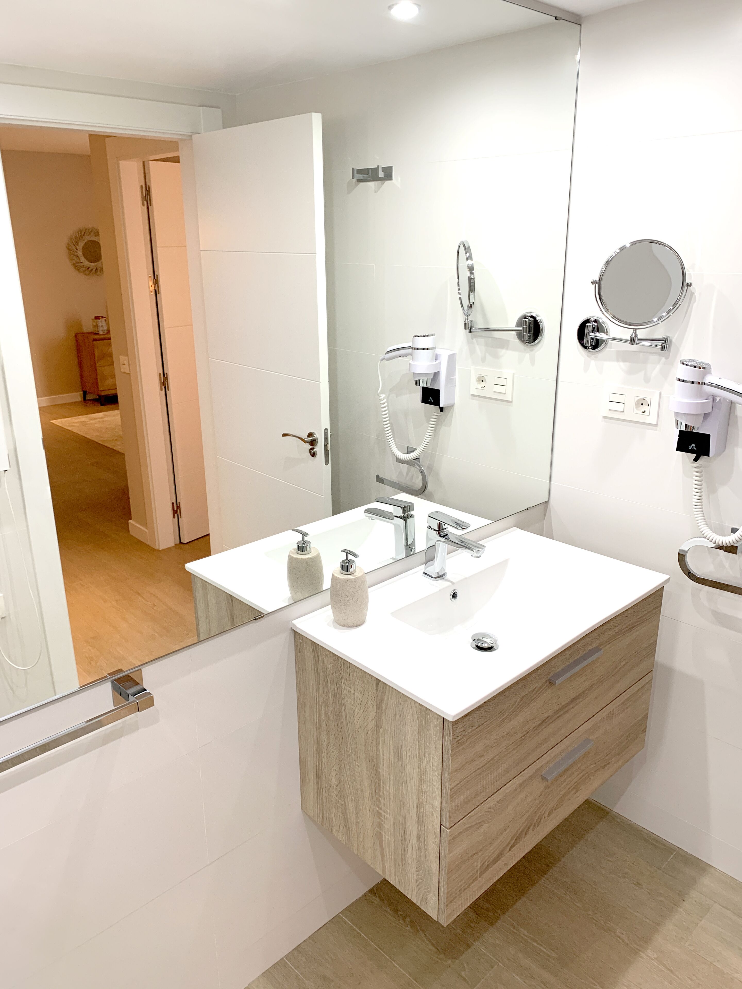 Un baño moderno con tocador doble, un espejo grande y un secador de pelo montado en la pared.