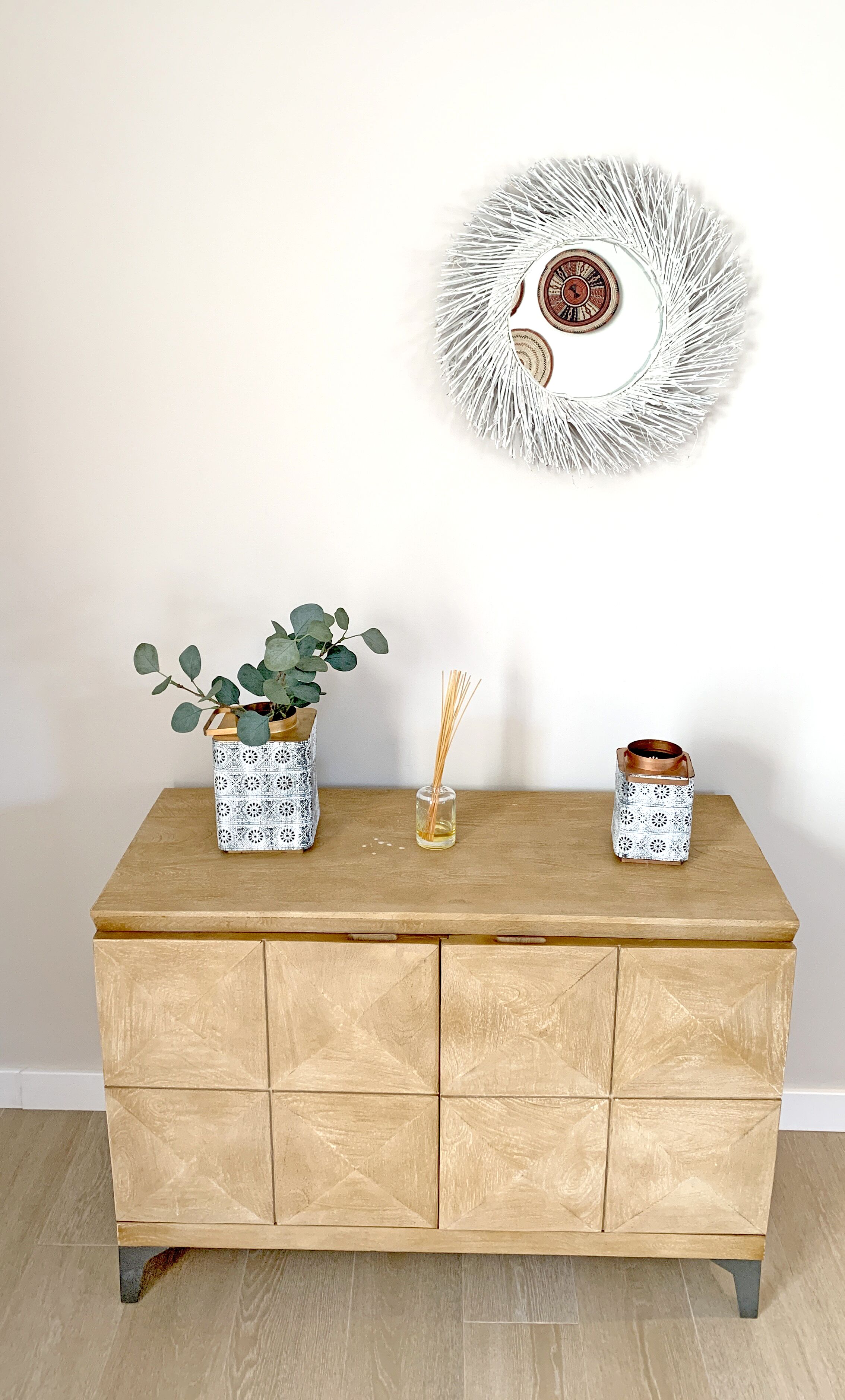 A wooden dresser with three decorative items: a potted plant, a reed diffuser, and a small container.