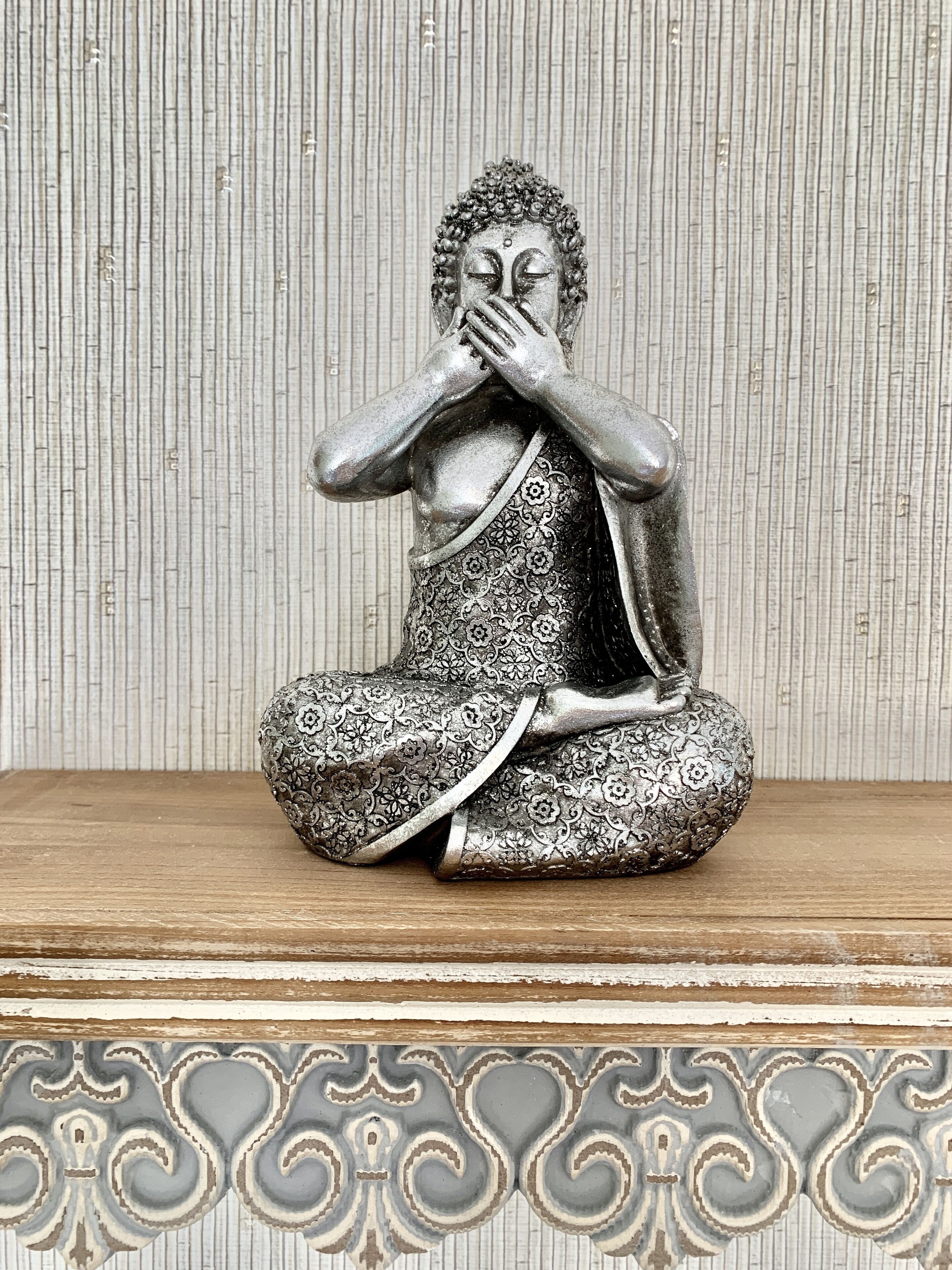A statue of a seated figure with a patterned robe, placed on a wooden surface with a decorative border.