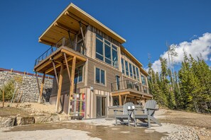 Une cabane en bois à plusieurs étages, dotée d’un balcon, d’un mur en pierre et offrant une vue dégagée sur la forêt environnante.