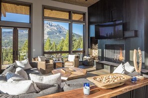 Un salon moderne doté d’une cheminée, de grandes fenêtres et offrant une vue imprenable sur les montagnes.