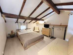 A bedroom with a bed, a chair, a dresser, a TV, and a drying rack.