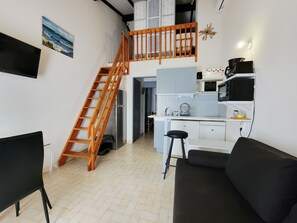 A compact living space with a kitchen, dining area, and a loft bedroom with a wooden staircase.