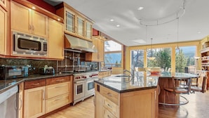 A modern kitchen with wooden cabinets, stainless steel appliances, and a large island with a sink. - Ski-In/Ski-Out House | Hot Tub | Views (Copper Mountain)