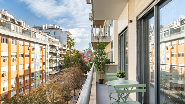 Un balcon avec une table et des chaises, donnant sur un paysage urbain avec des immeubles et des arbres.