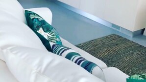 Un salon moderne avec un canapé blanc, un coussin à motifs et une cuisine en arrière-plan.