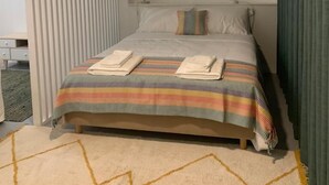 Un lit bien fait, avec une literie et des serviettes à rayures, une lampe de chevet et un tapis à motifs géométriques.