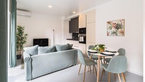 Un salon moderne avec un canapé gris, une table à manger et des chaises, un téléviseur et une plante en pot.