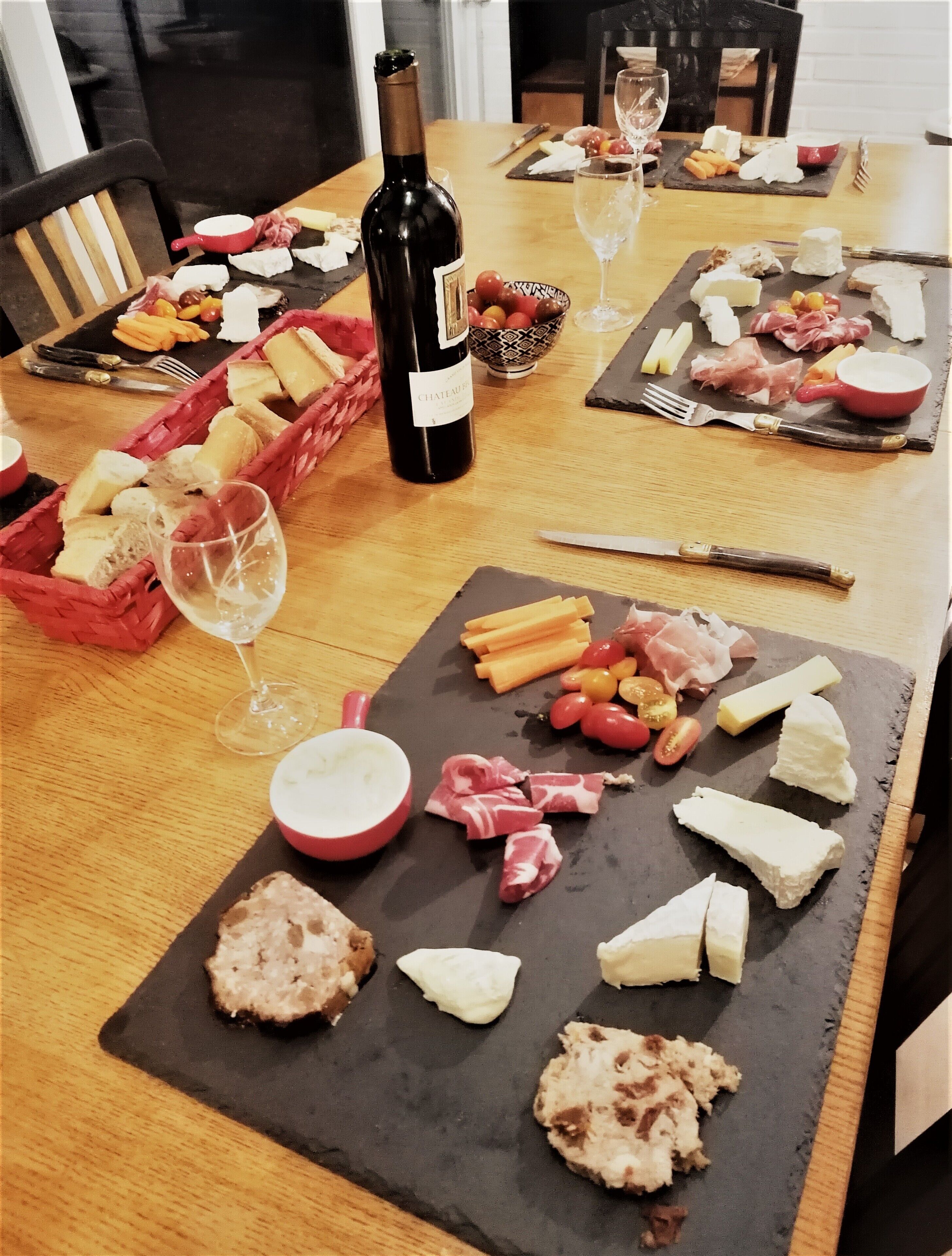 A wooden table with various cheeses, meats, and fruits, accompanied by wine glasses and a bottle of wine.