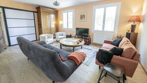 A living room with a sofa, armchair, coffee table, TV, and a lamp. - Chambres d'hôtes Au Chat Verrier, espace bien-être (Bagneaux-sur-Loing)