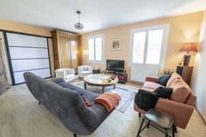 Una sala de estar con sofá, sillón, mesa de centro, televisión y lámpara.