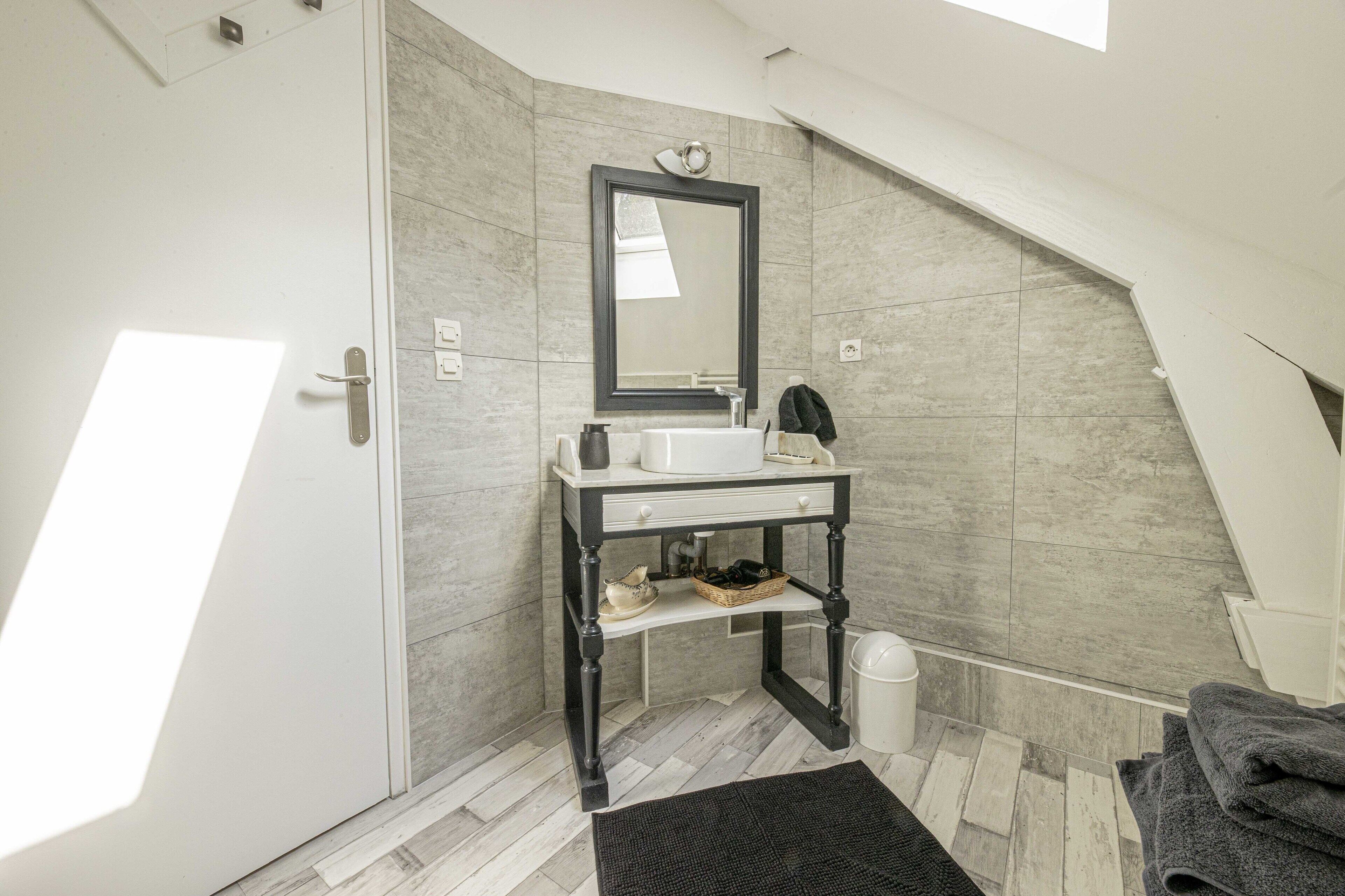 Un baño moderno con un lavamanos blanco, tocador de madera oscura y un espejo grande.