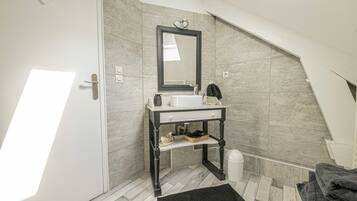 Un baño moderno con un lavamanos blanco, tocador de madera oscura y un espejo grande.