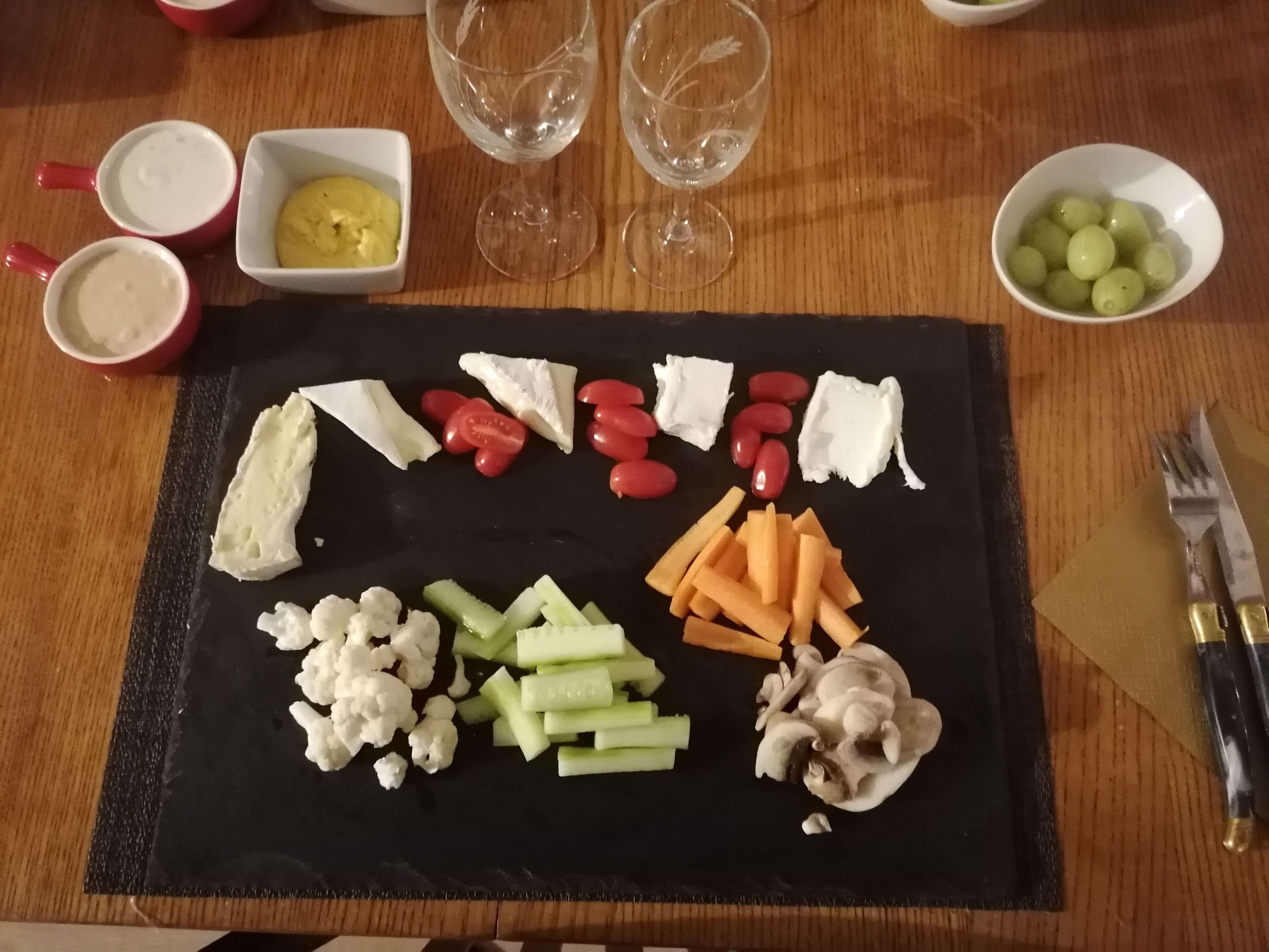 A charcuterie board with various cheeses, fruits, and vegetables on a black slate.