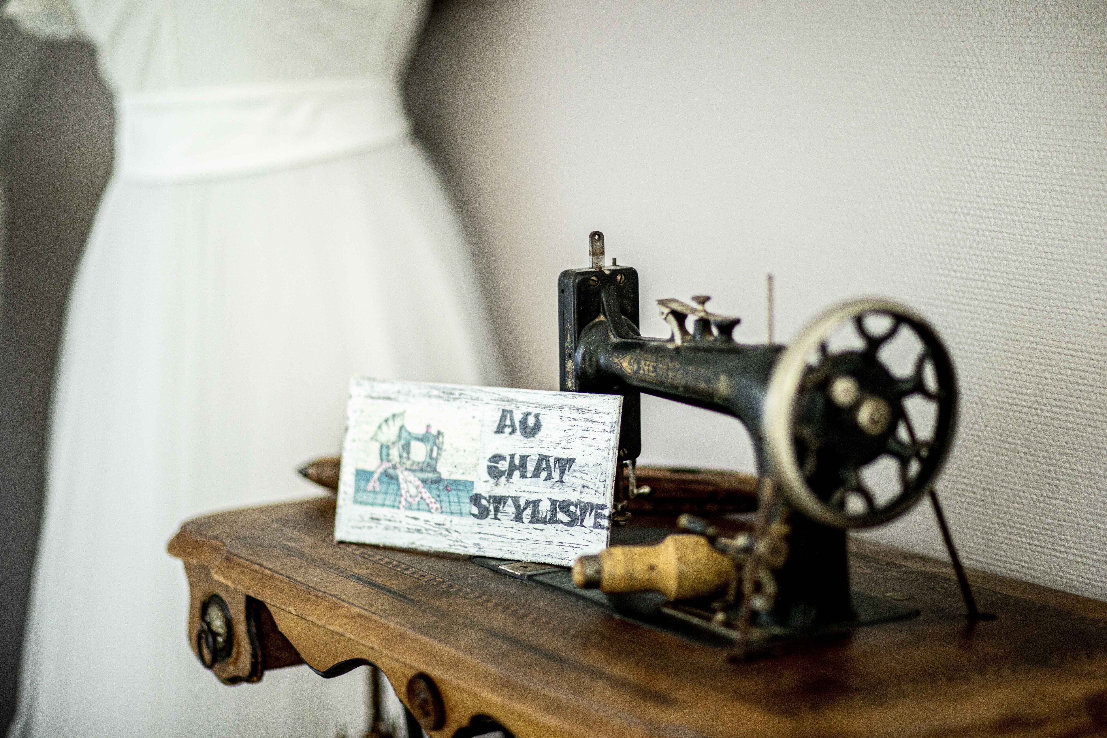 An antique sewing machine with a sign that reads "AU SHAW STYLISTE" on a wooden table.