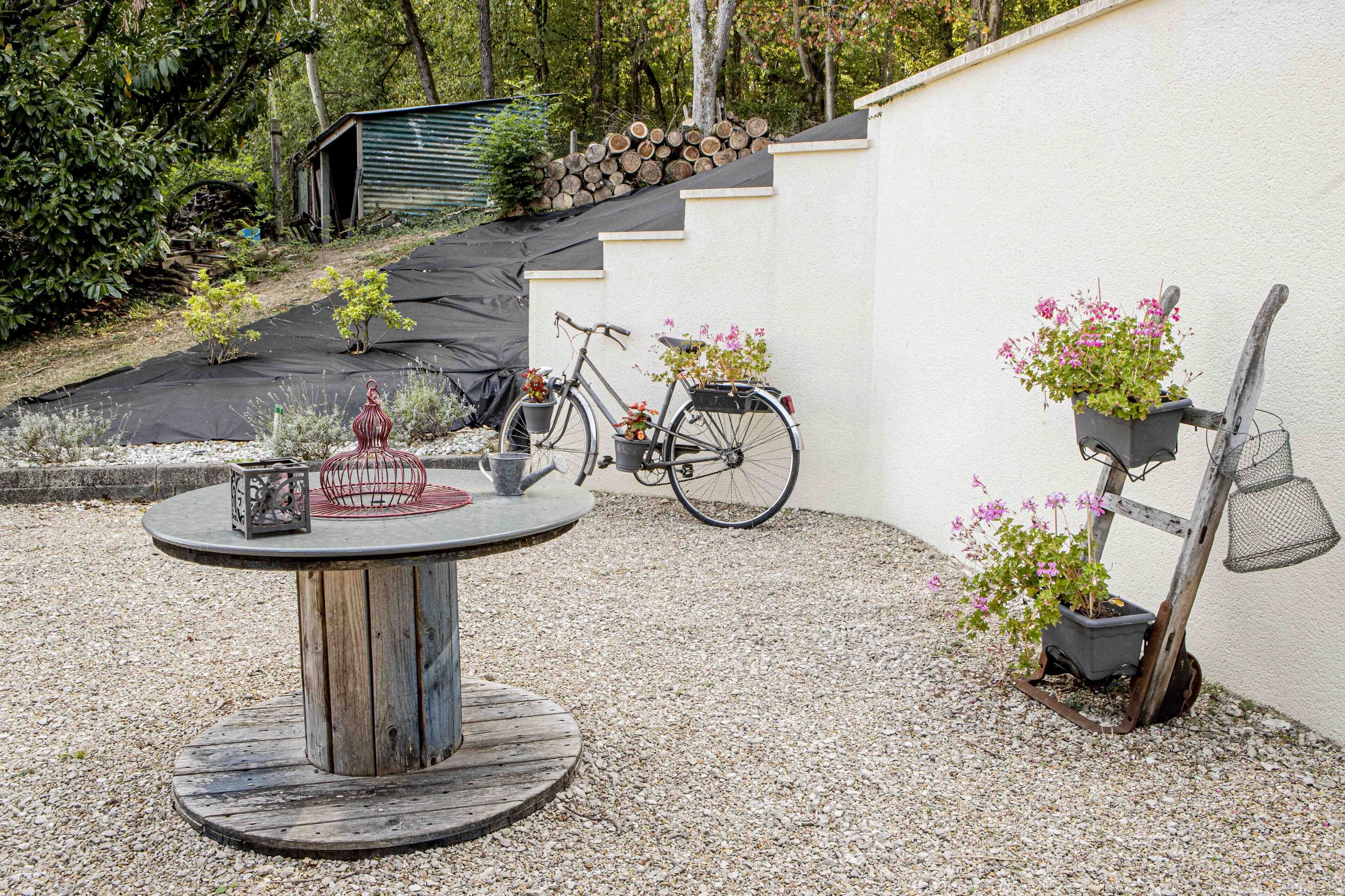 A garden patio with a round wooden table, a bicycle, and potted plants.