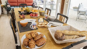 A breakfast table with croissants, bread, fruits, and a coffee mug. - Chambres d'hôtes Au Chat Verrier, espace bien-être (Bagneaux-sur-Loing)