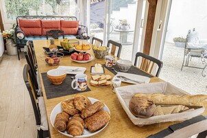 Una mesa de desayuno con cruasanes, pan, frutas y una taza de café.