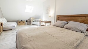 A bedroom with a large bed, a crib, a wooden nightstand, a wicker basket, and a wall-mounted lamp. - Chambres d'hôtes Au Chat Verrier, espace bien-être (Bagneaux-sur-Loing)