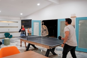 Ett bordtennisbord i ett modernt rum med en glasdörr, en stol och ett bord.