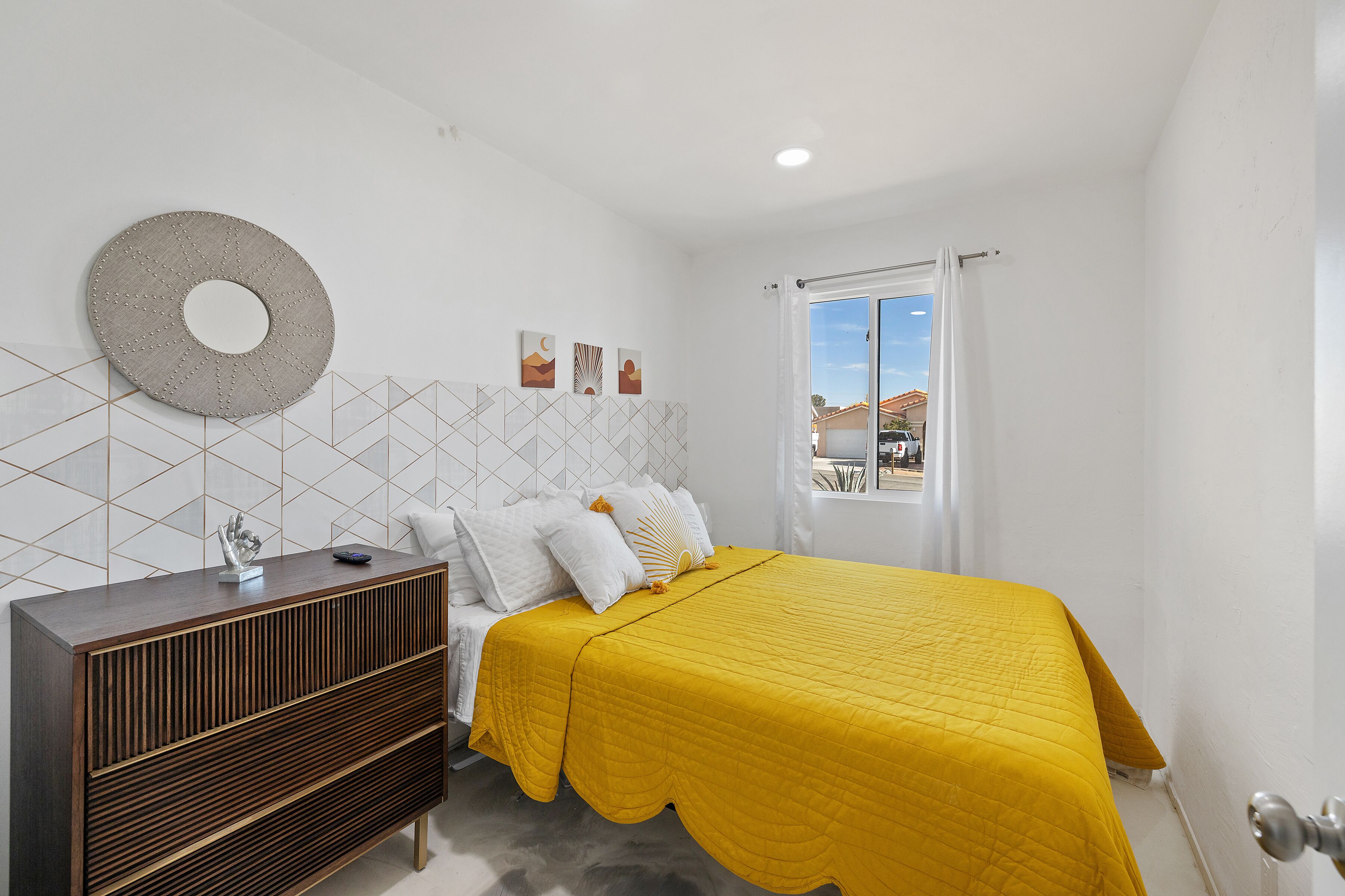 Une chambre à coucher comprenant un lit, une commode et un grand miroir rond fixé au mur.