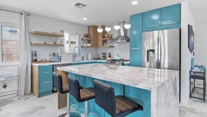 A modern kitchen with teal cabinets, a marble island, and bar stools. - Aquarium Pool Window • Private Heated Pool & Spa  • Mini Golf • Fire Pit • Bocce (Desert Hot Springs)