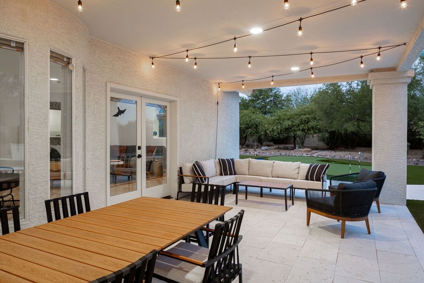 Une terrasse extérieure avec une table en bois, des chaises, un canapé et des guirlandes lumineuses.