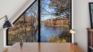 A room with a large window overlooking a lake and autumn trees.