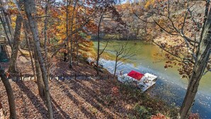 A dock with a red canopy extending over a calm body of water, surrounded by trees with autumn foliage.