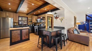 A modern kitchen with wooden cabinetry, a central island with stools, and a dining area with a sofa.