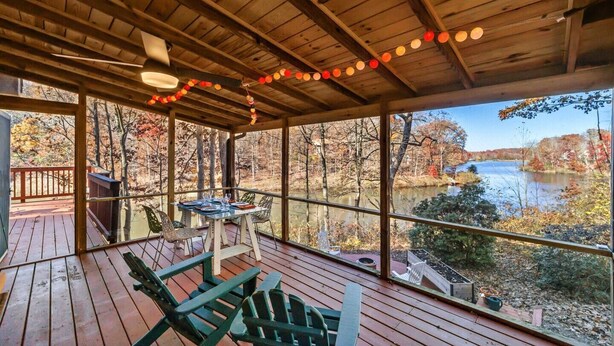 A covered deck with a table and chairs, overlooking a river and autumn foliage.