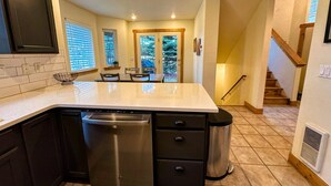 A kitchen with a dishwasher, a sink, and a trash can. There is a dining area with a table and chairs.