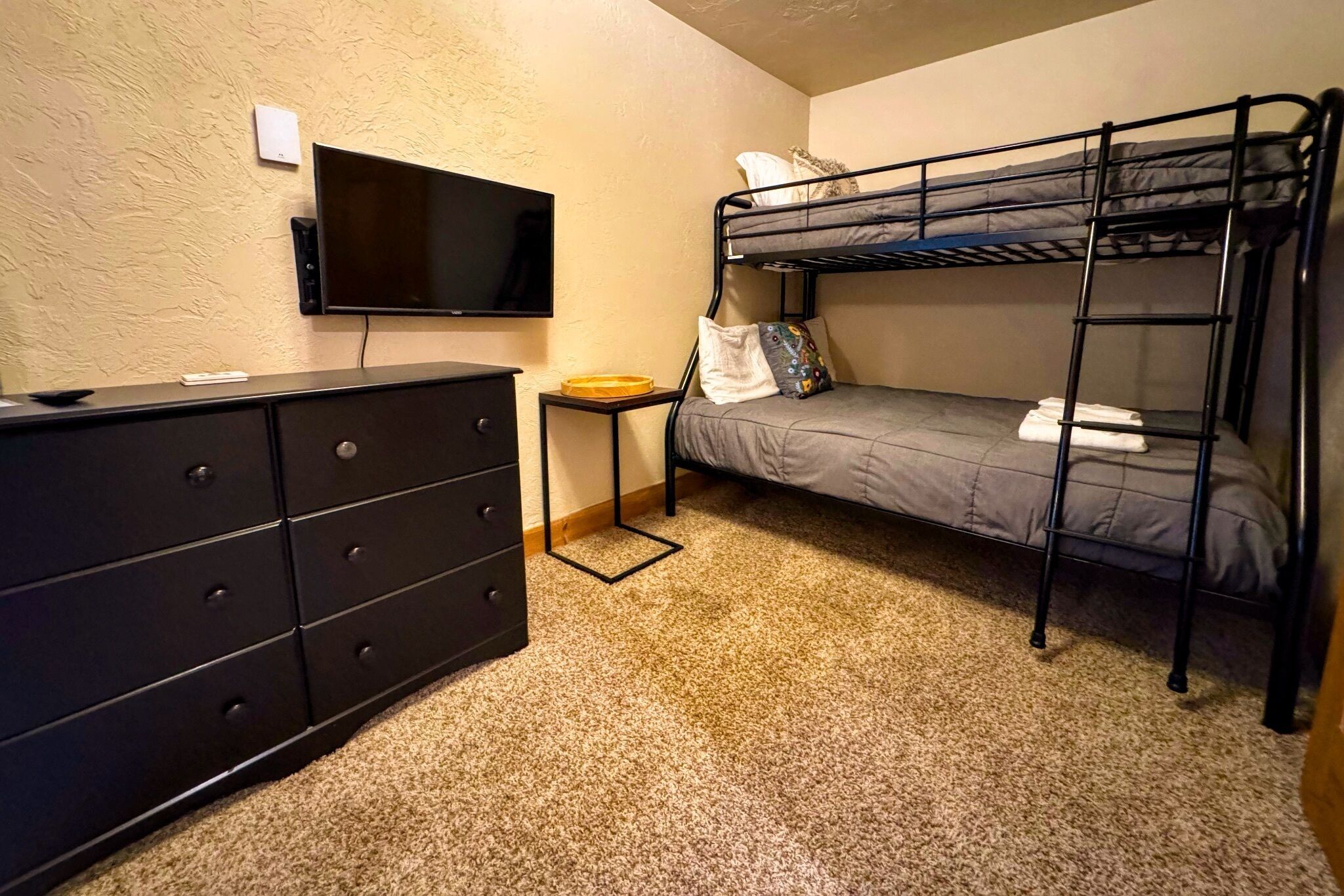 Ein kleines Zimmer mit Etagenbett, Kommode, Fernseher und kleinem Tisch.