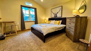A bedroom with a bed, a desk, a chair, a dresser, a ceiling fan, a window, and a framed picture on the wall.