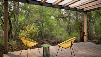 An outdoor wooden deck with two yellow chairs and a green table, surrounded by trees.