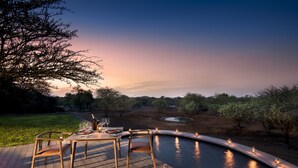 A dining area with a pool, wooden deck, and outdoor lighting. - Mbazo Safaris (Pilanesberg National Park)