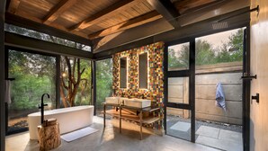 A modern bathroom with a large bathtub, a wooden vanity, and a colorful mosaic wall. - Mbazo Safaris (Pilanesberg National Park)