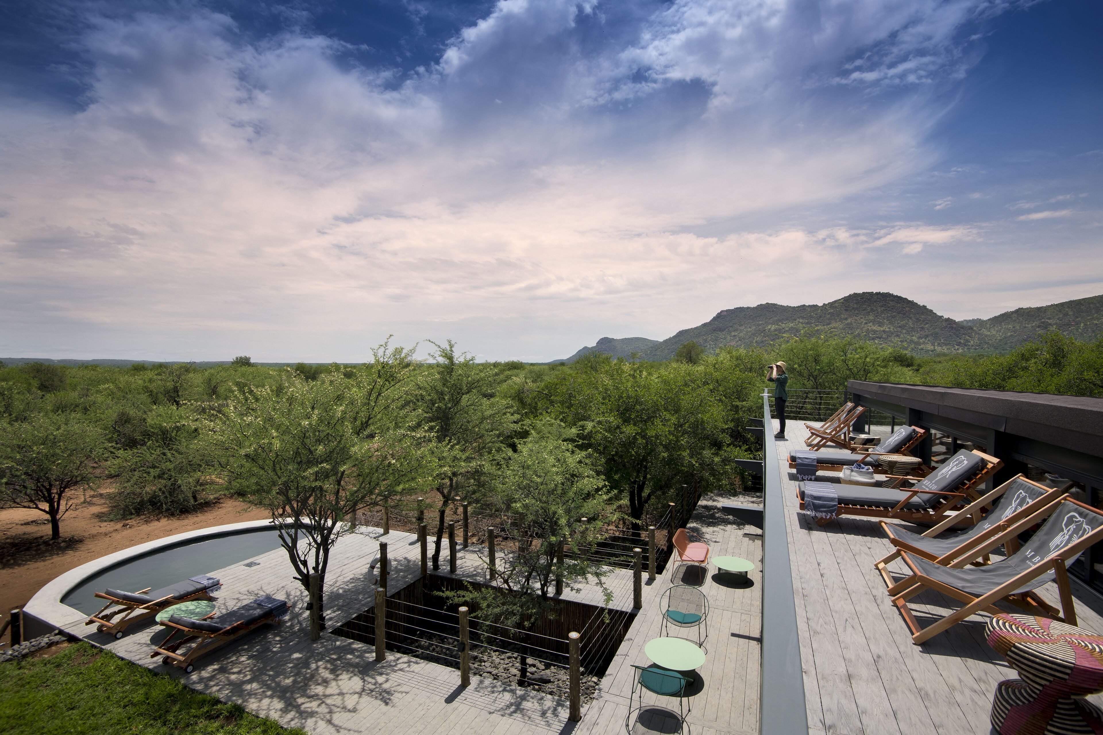 Área de piscina no terraço com espreguiçadeiras e uma piscina pequena, cercada por árvores e montanhas ao fundo.