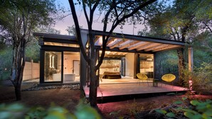 A modern house with a glass facade, a wooden deck, and a seating area with yellow chairs. - Mbazo Safaris (Pilanesberg National Park)