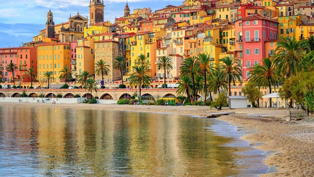 A coastal cityscape with colorful buildings, a waterfront promenade, and palm trees. - 2 Pièces 50m² Ensoleillés + 2 Terrasses BBC (Menton)