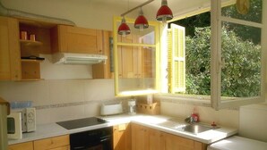 A compact kitchen with wooden cabinets, a microwave, a toaster, a sink, and a washing machine. - 2 Pièces 50m² Ensoleillés + 2 Terrasses BBC (Menton)