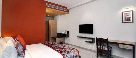 A hotel room with a bed, a desk, a chair, a TV, and a wardrobe.