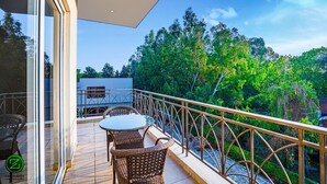 Balcón con mobiliario de mimbre y baranda de vidrio con vista a un jardín exuberante.
