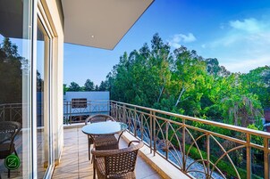 Balcón con mobiliario de mimbre y baranda de vidrio con vista a un jardín exuberante.