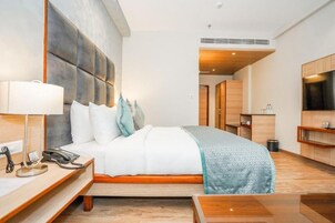 Una habitación de hotel moderna con una cama grande, una mesita de noche con lámpara, un teléfono y un cabecero de madera.